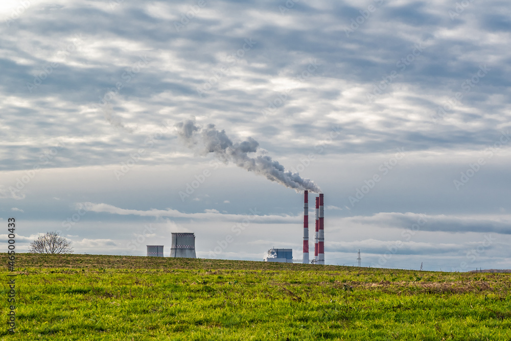 Green field against the background of clouds and blue sky, behind it a thermal power plant with smoking chimneys