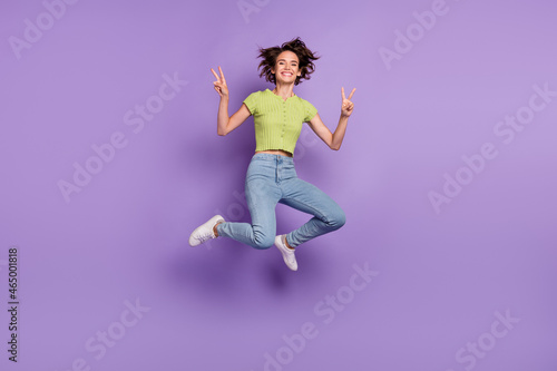 Photo of beautiful pretty young lady wear green t-shirt smiling jumping high showing v-signs isolated violet color background