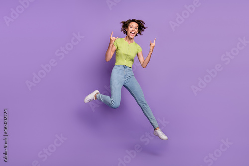 Photo of sweet rude young woman dressed green t-shirt jumping showing hard rock signs isolated purple color background © deagreez
