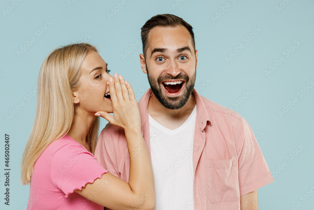 Young couple two friends family man woman in casual clothes whisper gossip and tells secret behind her hand sharing news together isolated on pastel plain light blue color background studio portrait. Young couple two friends family man woman in casual clothes whisper gossip and tells secret behind her hand sharing news together isolated on pastel plain light blue color background studio portrait.