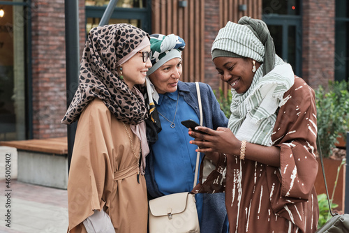 Muslim women talking to their friend while she reading a message on the phone and smiling during their meeting outdoors
