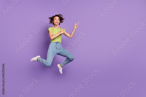 Photo of pretty impressed young lady wear green t-shirt pointing fingers empty space jumping isolated violet color background