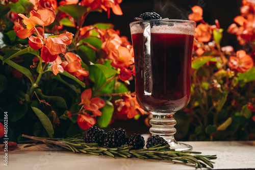 Blackberry mulled wine with rosemary in a glass cup on flowers background