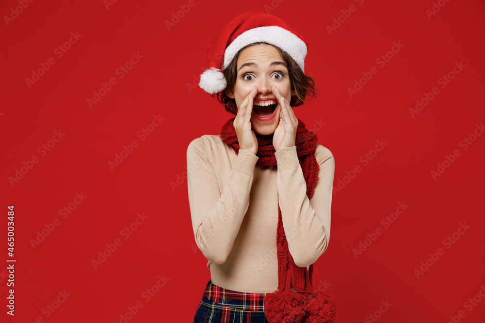 Young woman 20s wear Santa Claus Christmas red hat scream hot news about sales discount with hands near mouth isolated on plain red background studio portrait. Happy New Year 2022 celebration concept. Young woman 20s wear Santa Claus Christmas red hat scream hot news about sales discount with hands near mouth isolated on plain red background studio portrait. Happy New Year 2022 celebration concept.