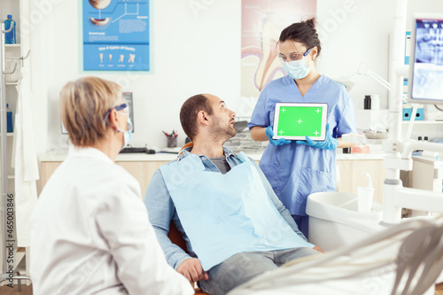 Sick patient looking at touchscreen gadget while speaking with stomatology senior doctor. Medical nurse explaining using with mock up green screen chroma key digital tablet with isolated display