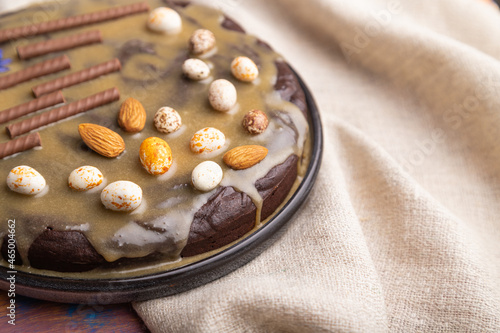 Homemade chocolate brownie cake with caramel cream and almonds with cup of coffee on a colored wooden background. Side view, selective focus.