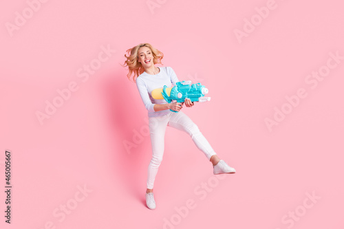 Full size photo of charming young funky woman shoot water gun empty space vacation isolated on pink color background