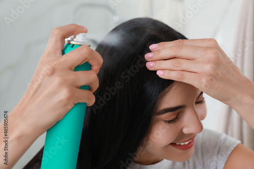 Woman applying dry shampoo onto her hair indoors, closeup photo