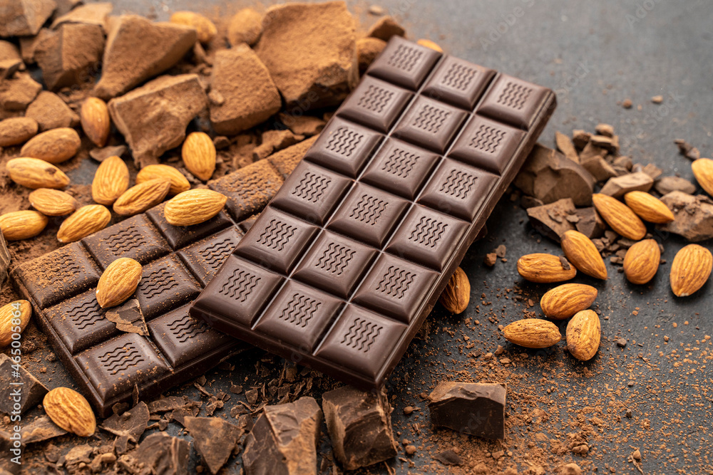 Store Cooking chocolate bars with almonds handmade sweets. Composition of bars and pieces of dark almond chocolate on a black background, top view. Pastry craft on the table Store Cooking chocolate bars with almonds handmade sweets. Composition of bars and pieces of dark almond chocolate on a black background, top view. Pastry craft on the table