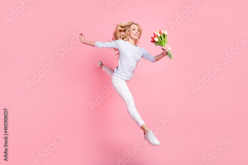 Full size photo of happy cheerful young,woman jump up look flowers isolated on pink color background