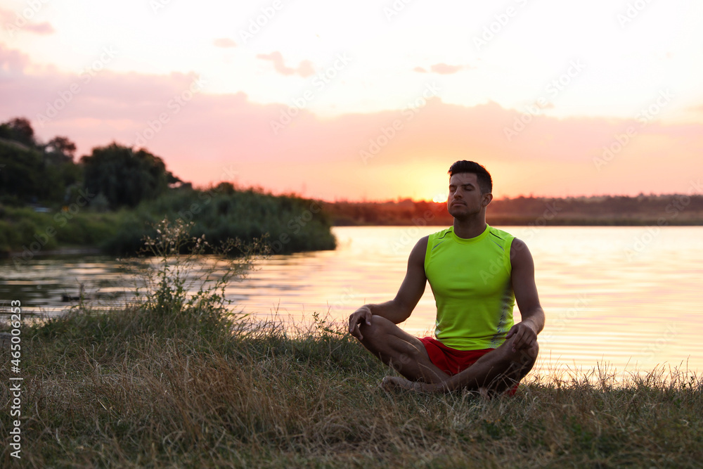 Man meditating near river in twilight. Space for text