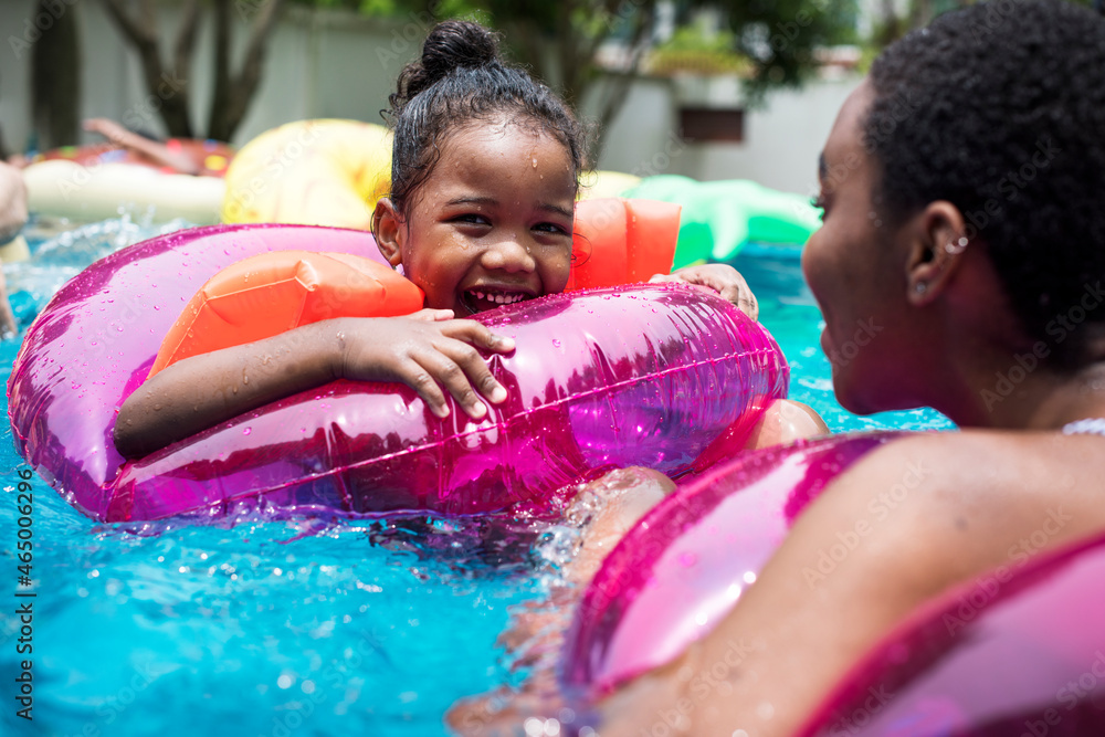 Closeup of black mother and daughter enjoying the pool with inflatable tubes - obrazy, fototapety, plakaty 