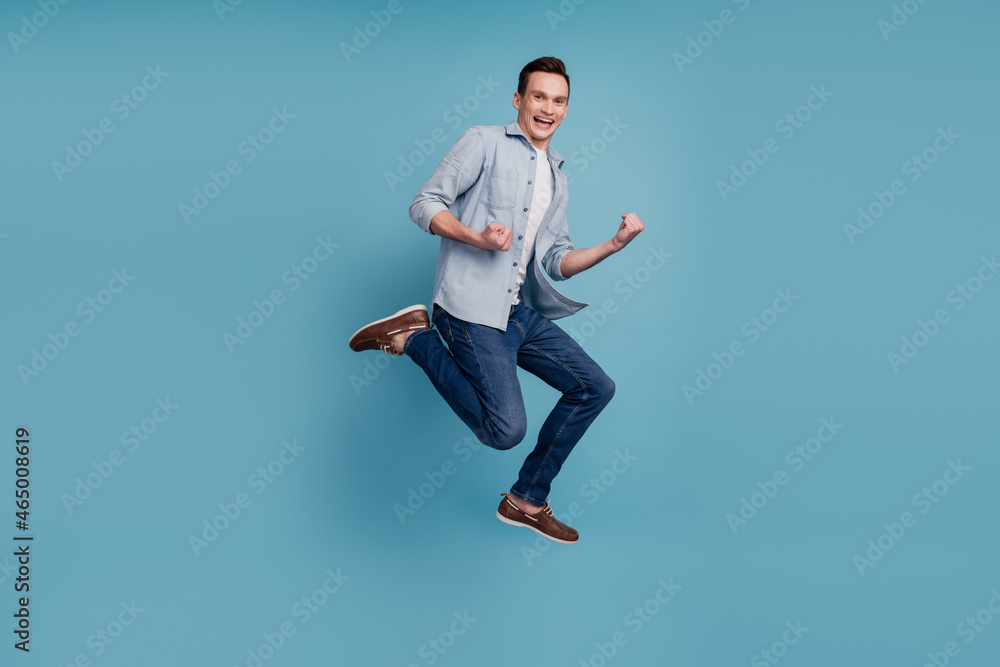Full size profile side photo of young man celebrate winner jump go isolated over blue color background Full size profile side photo of young man celebrate winner jump go isolated over blue color background