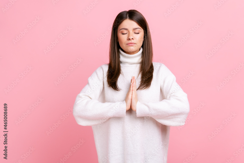 Calm relaxed female standing with closed eyes, breathing, doing yoga exercising, feeling harmony, wearing white casual style sweater. Indoor studio shot isolated on pink background. Calm relaxed female standing with closed eyes, breathing, doing yoga exercising, feeling harmony, wearing white casual style sweater. Indoor studio shot isolated on pink background.