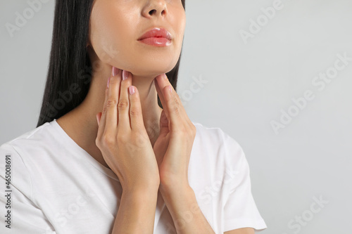 Young woman doing thyroid self examination on light background, closeup