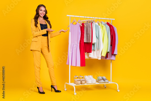 Photo of shiny charming young woman dressed suit blazer advising buying new clothes smiling isolated yellow color background