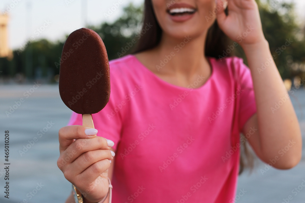 Young woman holding ice cream glazed in chocolate on city street, closeup Young woman holding ice cream glazed in chocolate on city street, closeup