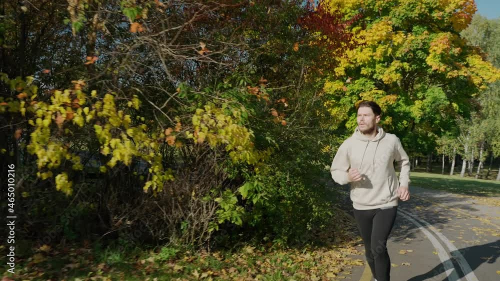 Man running on jogging track at the city park in sunny autumn morning, front view. Man having a morning run. Running at the empty city park. High quality 4k footage Man running on jogging track at the city park in sunny autumn morning, front view. Man having a morning run. Running at the empty city park. High quality 4k footage