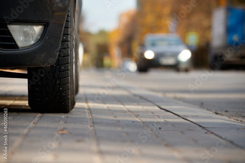 A car with winter wheels and metal spikes standing on the side of the road against the background of passing cars and bright colors of autumn. Preparing for the winter season, the first frost and snow