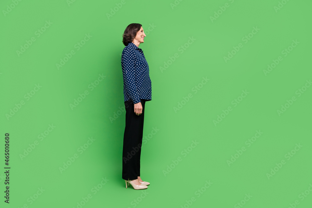 Full length profile photo of old lady wear shirt pants high heels isolated on green color background Full length profile photo of old lady wear shirt pants high heels isolated on green color background