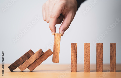 Fotografie Hand pull out wooden block to prevent and stop falling domino ,It is a symbol of protection against damage or stop loss for crisis management concept