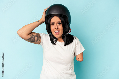 Young caucasian woman with one arm wearing a motorcycle helmet isolated o blue background being shocked, she has remembered important meeting.