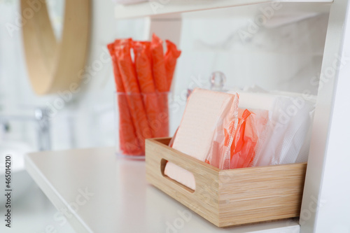 Organizer with tampons and menstrual pads on shelving unit in bathroom. Feminine hygiene products