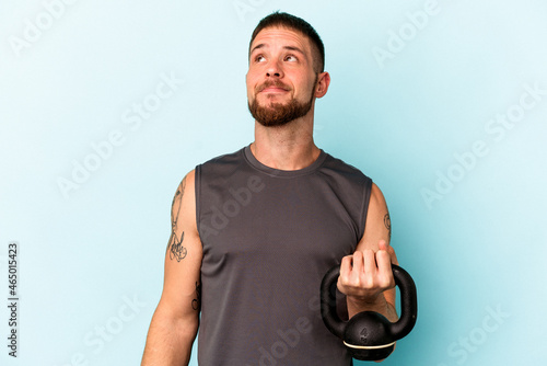 Young caucasian man holding ketlebell isolated on blue background dreaming of achieving goals and purposes photo