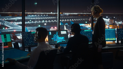 Female and Male Air Traffic Controllers with Headsets Talk in Airport Tower at Night. Office Room Full of Desktop Computer Displays with Navigation Screens, Airplane Flight Radar Data for Controllers.