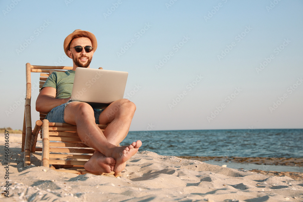 Man working with laptop in deck chair on beach. Space for text