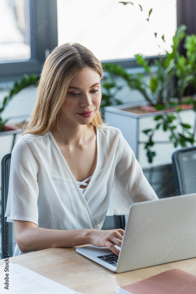 Pretty businesswoman using laptop near paper folder in office Pretty businesswoman using laptop near paper folder in office