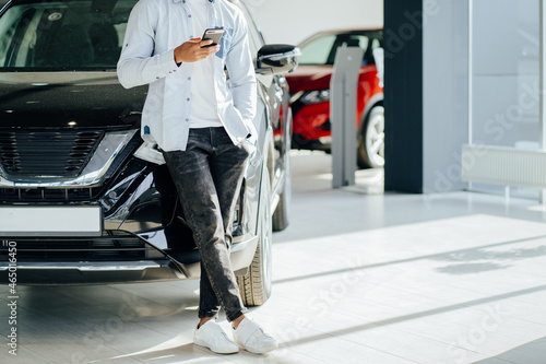 African man standing at auto salon and using smartphone