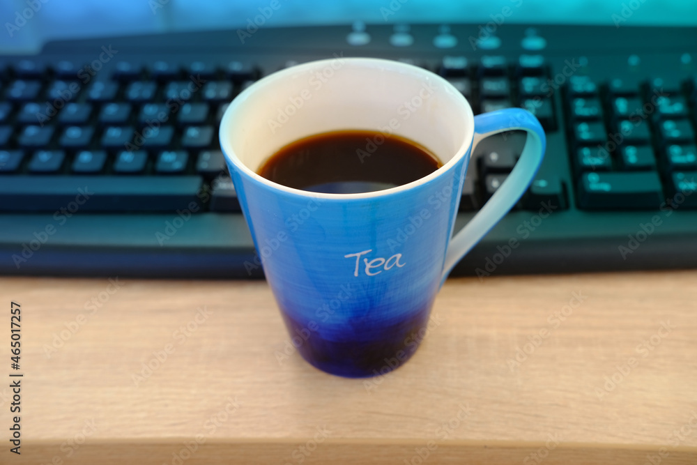 closeup of computer keyboard, blue large cup of coffee, tea suddenly spills, hot liquid spoils equipment, concept of tea time, benefits and the challenges of working from home closeup of computer keyboard, blue large cup of coffee, tea suddenly spills, hot liquid spoils equipment, concept of tea time, benefits and the challenges of working from home