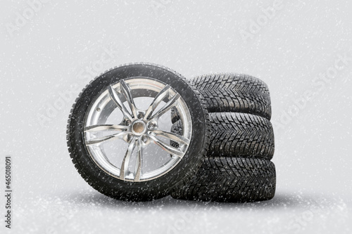 winter studded tires, a set of friction winter wheels with aluminum alloy wheels on a white background. falling snow is a safety concept about seasonal tire change for safety on the road in icy photo