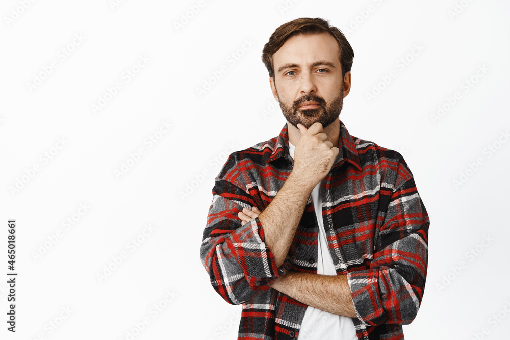 Image of thoughtful caucasian man looking serious at camera, thinking, making his decision at shop, standing over white background Image of thoughtful caucasian man looking serious at camera, thinking, making his decision at shop, standing over white background
