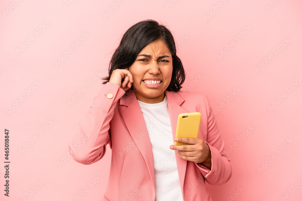 Young latin woman holding mobile phone isolated on pink background covering ears with hands. Young latin woman holding mobile phone isolated on pink background covering ears with hands.