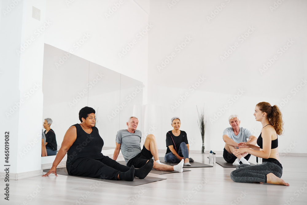 Group of senior people sitting on the floor and practicing yoga together with coach in the gym Group of senior people sitting on the floor and practicing yoga together with coach in the gym