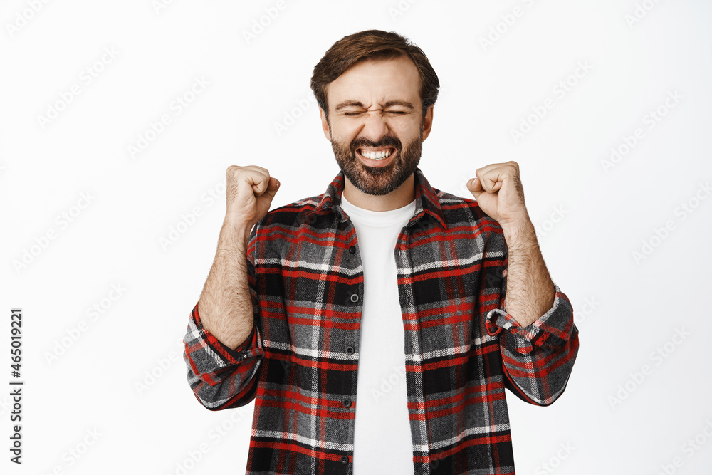 Ecstatic bearded guy winning and cheering, triumphing, clench fists and rejoicing, standing over white background Ecstatic bearded guy winning and cheering, triumphing, clench fists and rejoicing, standing over white background