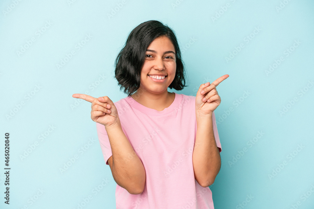 Young latin woman isolated on blue background pointing to different copy spaces, choosing one of them, showing with finger. Young latin woman isolated on blue background pointing to different copy spaces, choosing one of them, showing with finger.