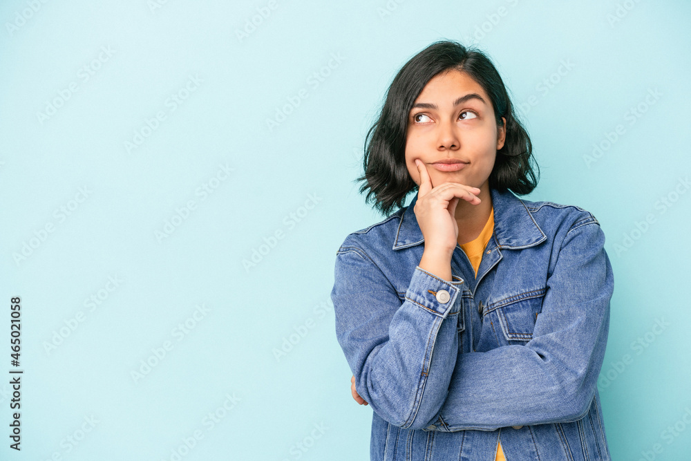 Young latin woman isolated on blue background relaxed thinking about something looking at a copy space. Young latin woman isolated on blue background relaxed thinking about something looking at a copy space.