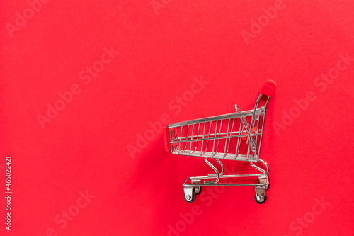 Grocery shopping cart with gift box on red background.