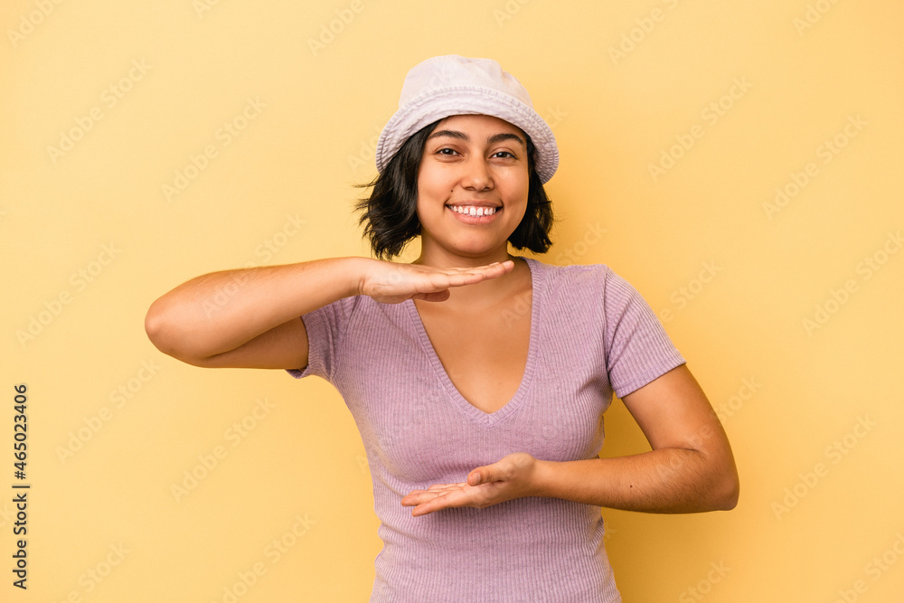 Young latin woman isolated on yellow background holding something with both hands, product presentation. Young latin woman isolated on yellow background holding something with both hands, product presentation.