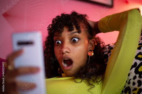 Multiracial young adult female looking shocked at a smartphone photo