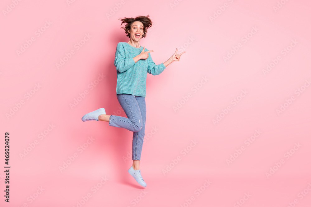 Full length photo of charming young woman point fingers empty space jump isolated on pink color background