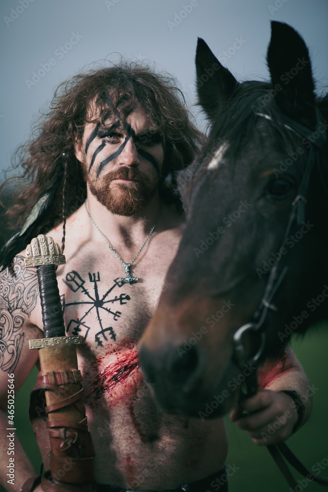 Medieval warrior berserk Viking portrait with tattoo on skin, cuts on body and braids in hair with weapons to attacks enemy. Concept historical photo