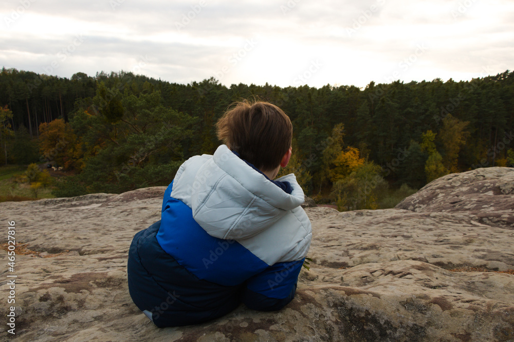 Young boy resting on the top of the rock overlooking spruce forest on cold autumn afternoon in Czech Republic, Bohemian Paradise Young boy resting on the top of the rock overlooking spruce forest on cold autumn afternoon in Czech Republic, Bohemian Paradise