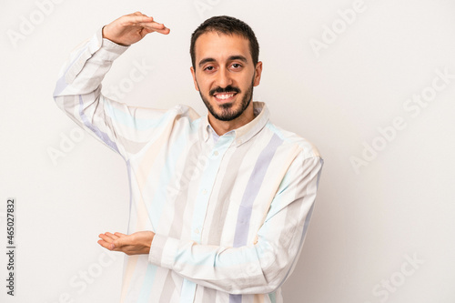 Young caucasian man isolated on white background holding something little with forefingers, smiling and confident.