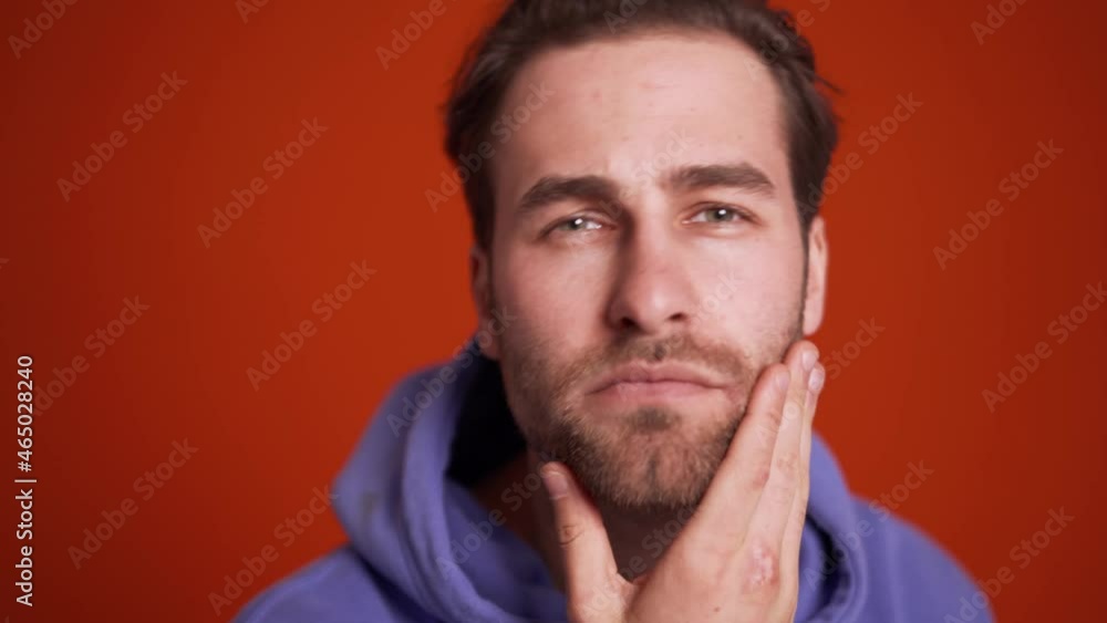 Close-up view of smiling man in the purple hoodie correct her appearance at the camera in orange studio Close-up view of smiling man in the purple hoodie correct her appearance at the camera in orange studio
