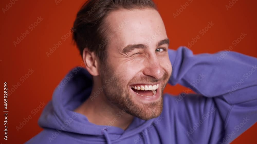 Close-up view of smiling man in the purple hoodie winking and pointing at the camera in orange studio Close-up view of smiling man in the purple hoodie winking and pointing at the camera in orange studio