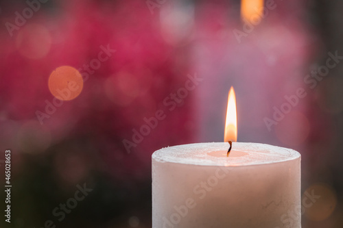 Close up photo of white burning candle on pink background.